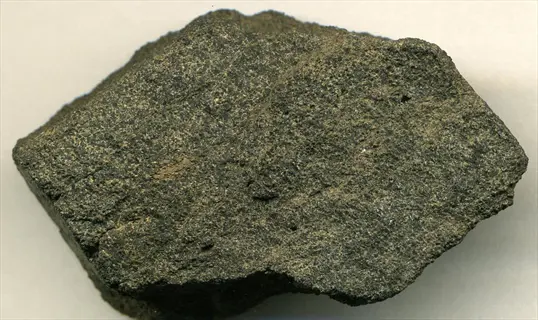 a rough dark rock phosphate mineral specimen on a light background