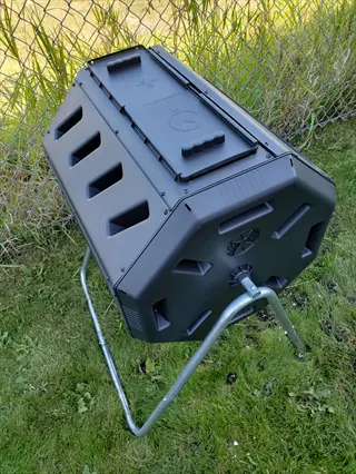 black compost tumbler on metal stand in a grassy yard