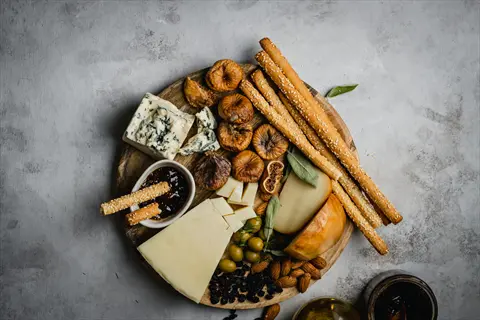dried figs platter with cheeses, breadsticks, olives, nuts, and jam on a wooden board