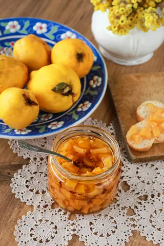 fig preserves jar with yellow fruit, spoon, bread slices, and decorative bowl on lace tablecloth