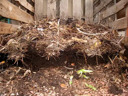 garden compost pile of dark soil, straw, and plant scraps in a wooden bin