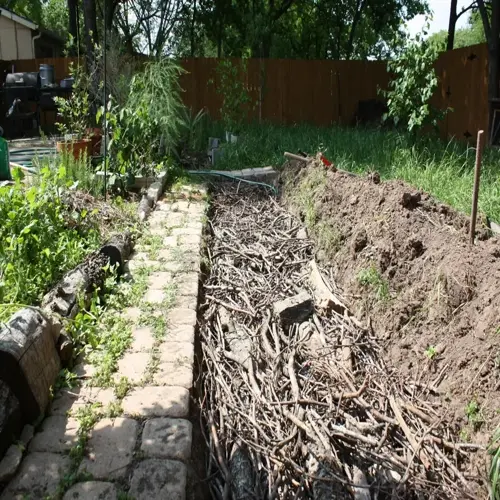 hugelkultur raised bed under construction with logs, branches, soil mound, and garden path