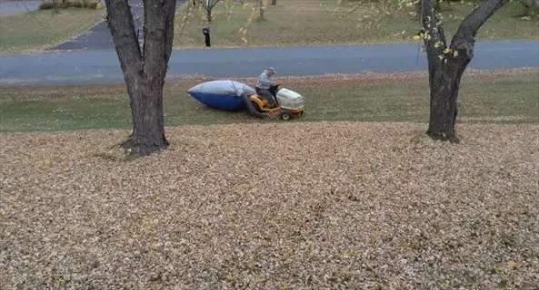 person on lawn tractor, leaves tarp driveway crushing fallen leaves