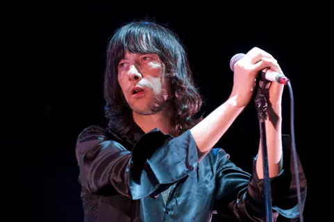primal scream singer performing live with a microphone on a dark stage