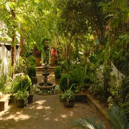 shaded perennial garden with fountain, brick paths, potted flowers, and lush trees